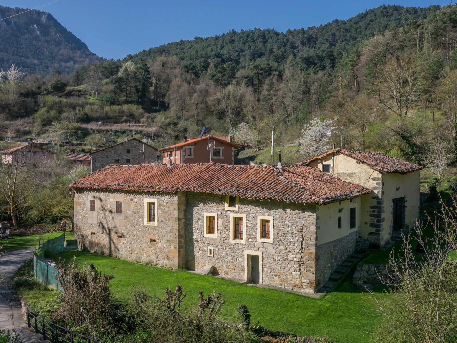 Casa de piedra con tejado de teja entre prados y montes